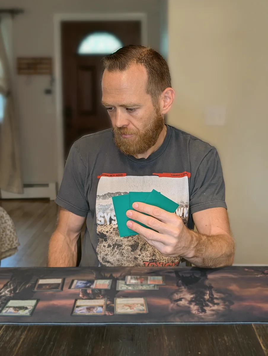 Chris studying a fanned hand of sleeved cards, head down in mid-playtest thought